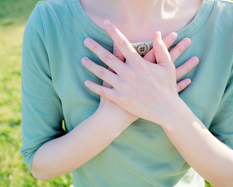 Young woman with hands on her heart. Heal trauma with NARM therapy in Texas