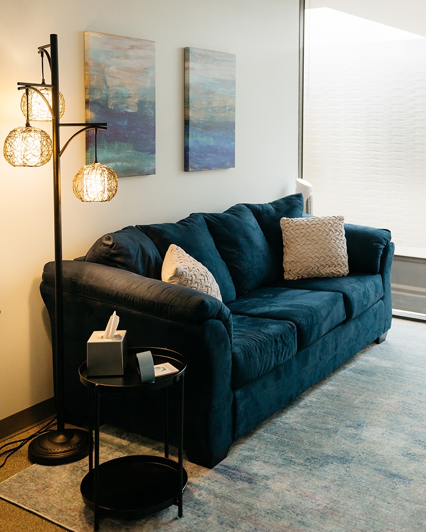 resilience_counseling_wellness_couch Blue couch with beige pillows, standing light and end table in therapy waiting room Houston Texas